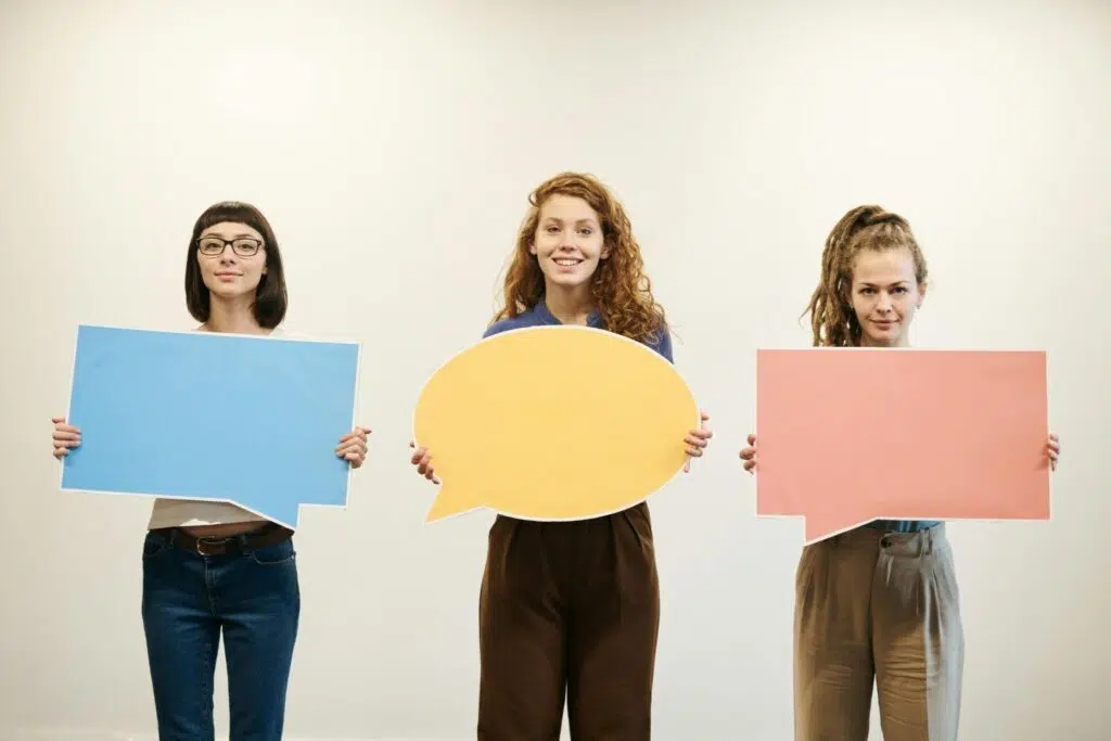 Three women holding colourful speech bubble signs
