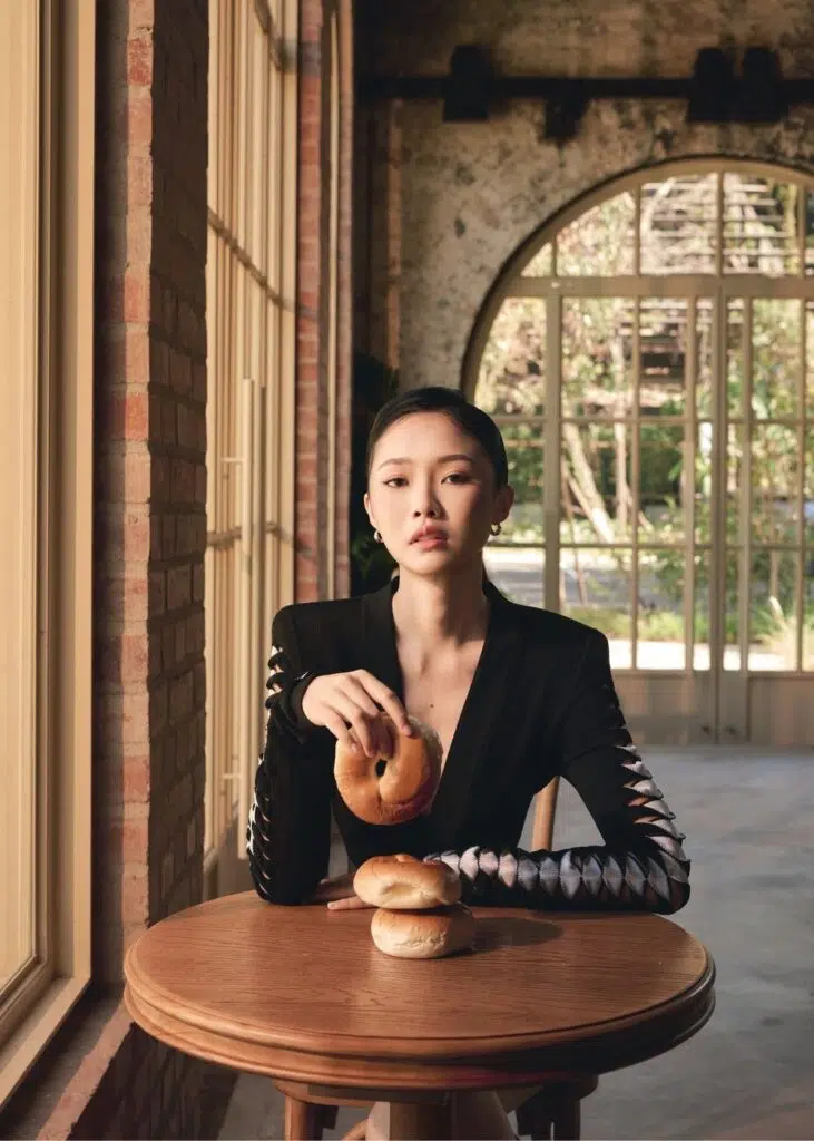 Claire Tan seated at a wooden café table holding a bagel