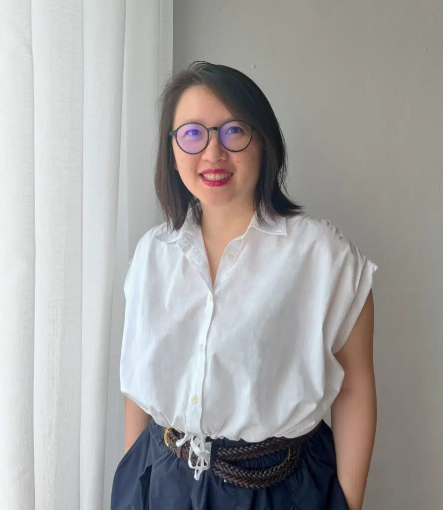 Koh Cha-Ly in a white blouse standing beside soft window light indoors