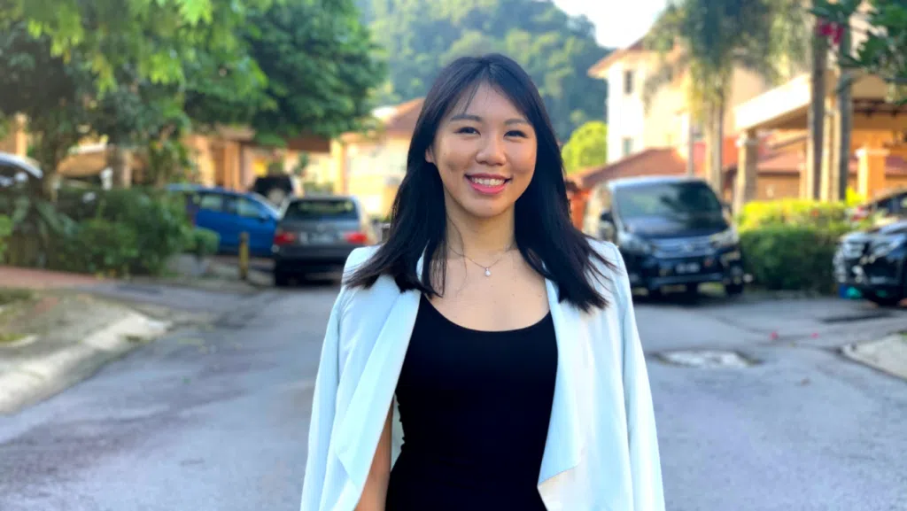 Michelle Chin in a white blazer standing on a quiet residential street.