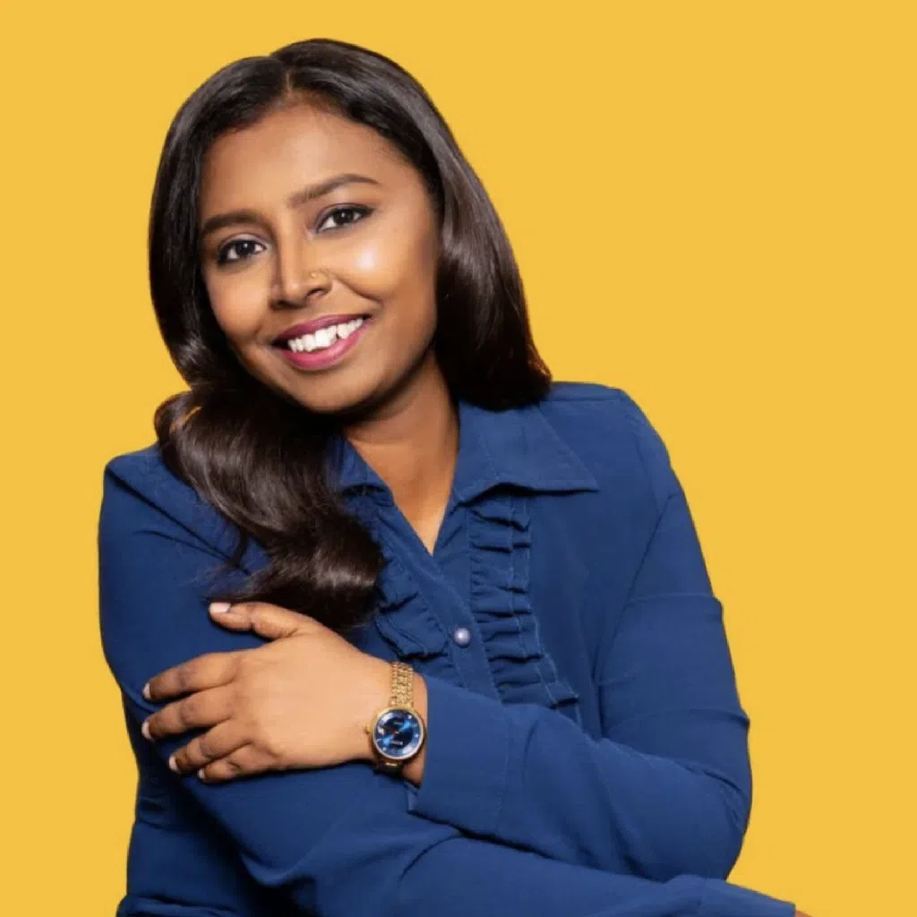 Gevitha Ananda Roe in a blue blouse against a bold yellow studio background