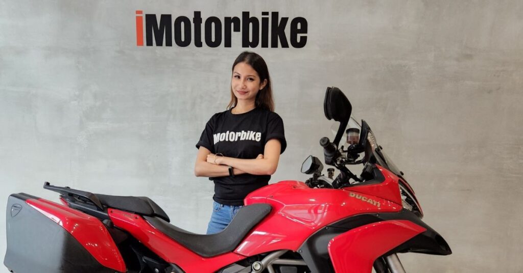 Sharmeen Looi standing beside a red motorcycle in a modern showroom